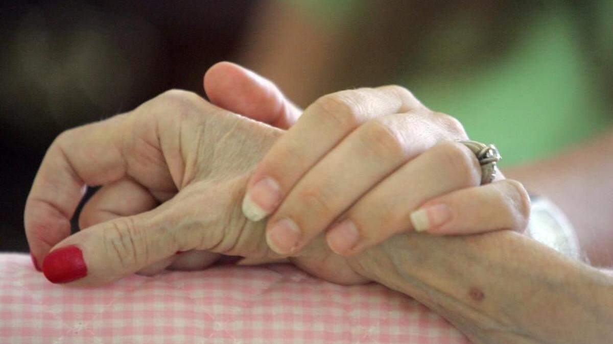 A hospice family support volunteer holds hands with her client in 2006.