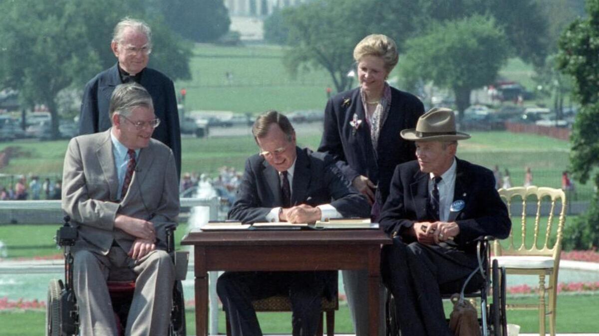 In this July 26, 1990 file photo, President George H. W. Bush signs the Americans with Disabilities Act during a ceremony on the South Lawn of the White House. Joining the president are, from left, Evan Kemp, chairman of the Equal Opportunity Employment Commission; Rev. Harold Wilke; Sandra Parrino, chairman of the National Council on Disability, and Justin Dart, chairman of The President's Council on Disabilities.