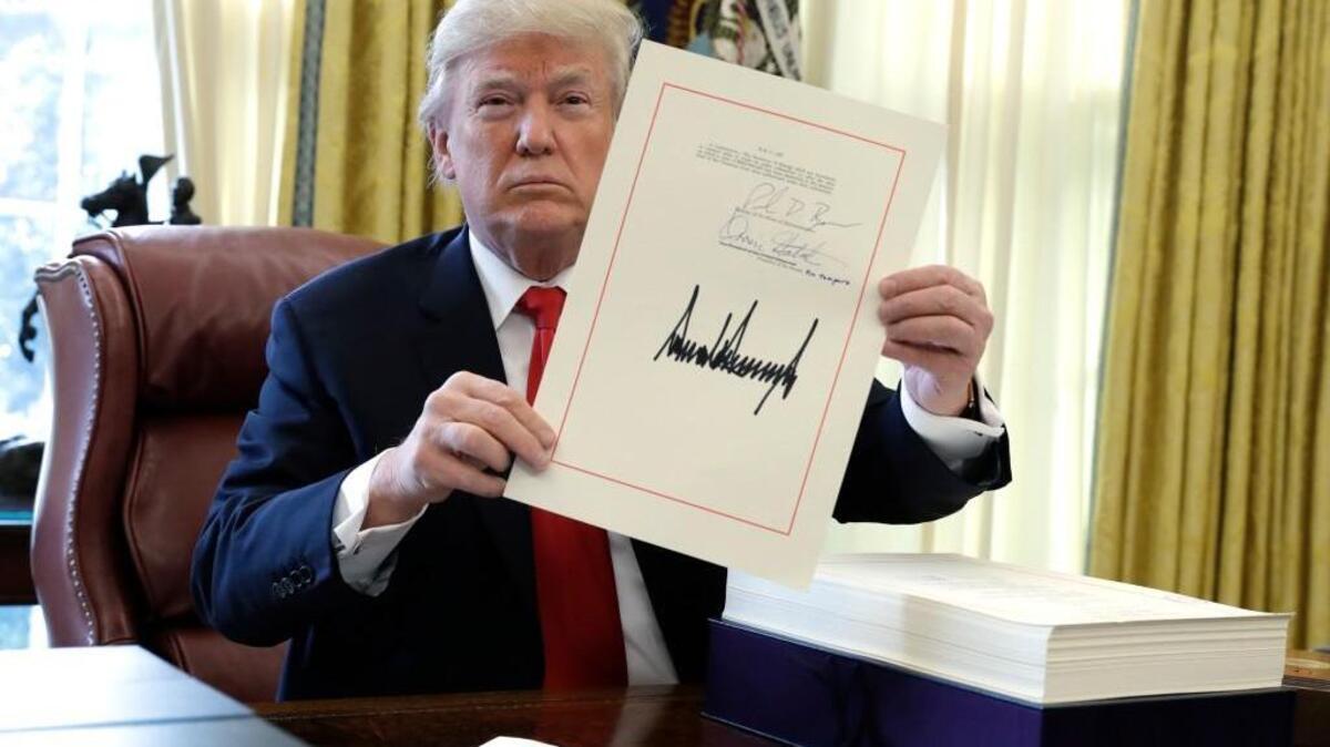 President Donald Trump displays the $1.5 trillion tax overhaul package he had just signed, Friday, Dec. 22, 2017, in the Oval Office of the White House in Washington. Trump touted the size of the tax cut, declaring to reporters in the Oval Office before he signed it Friday that "the numbers will speak."