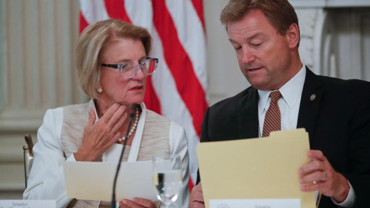 Sen. Shelley Moore Capito, R-W.Va., left, and Sen. Dean Heller, R-Nev., look over documents from a folder provided by the White House during a luncheon with President Donald Trump, Wednesday, July 19, 2017, in the State Dinning Room of the White House in Washington.