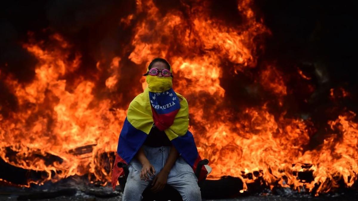 A Venezuelan opposition activist is backdropped by a burning barricade during a demonstration against President Nicolas Maduro in Caracas, on April 24.