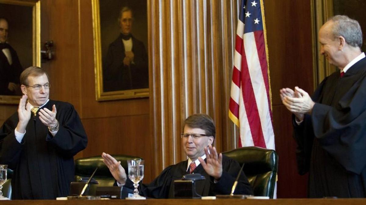 Chief Justce Mark Martin, center, gestures for Justice Robert Edmunds, left, and Paul Newby, right, to cease their applause as he takes his seat after he was sworn in as the Chief Justice of the N.C. Supreme Court during a ceremony held in downtown Raleigh on Jan. 5, 2015.