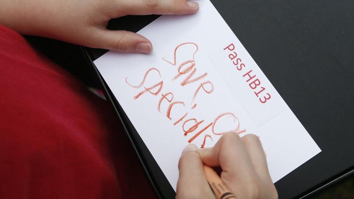A student works on a postcard to send to legislators during a rally at Halifax Mall in Raleigh, N.C. urging the North Carolina Senate to pass House Bill 13 Wednesday, April 19, 2017. School districts around the state say arts and PE programs are at risk because they lost their flexibility to fund them when state legislators lowered class sizes for kindergarten through third grade. School officials say HB13 would allow them to save arts and PE classes.