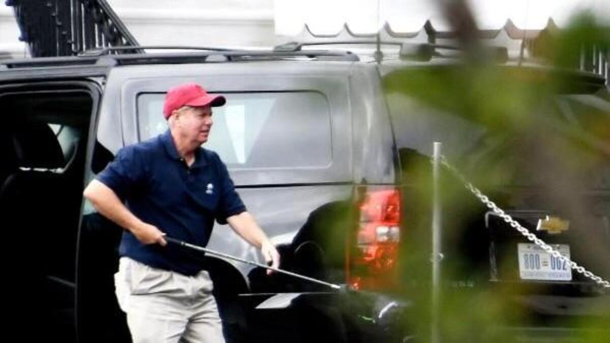 Senator Lindsey Graham (R-SC), left, carries one of his golf clubs as he leaves the presidential limo at the White House on October 14, 2017 in Washington, DC. U.S. President Donald Trump is seen at right talking on the phone. The two are returning after playing a round of golf.
