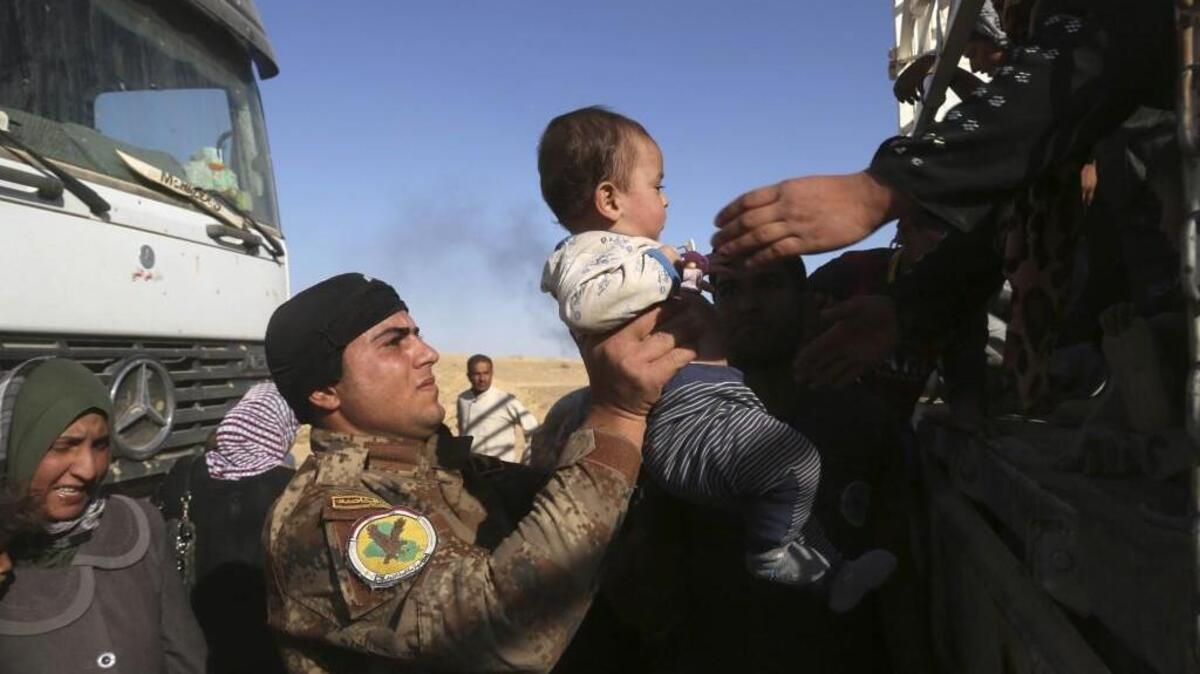 A member of elite counter terrorism forces helps women and children fleeing their homes in Iraq.