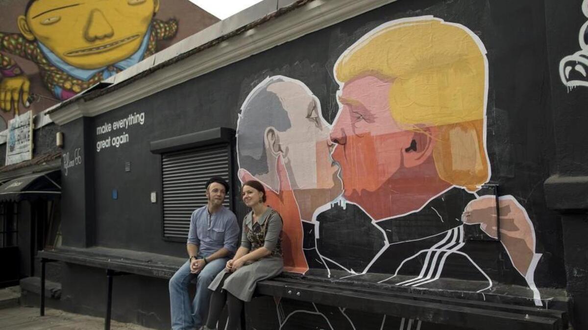 A couple sits in front of graffiti depicting Russian President Vladimir Putin, left, and Republican presidential candidate Donald Trump, on the walls of a bar in the old town in Vilnius, Lithuania.