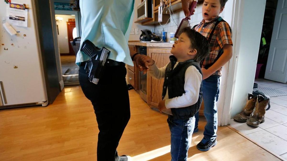A mother wears her usual gun on her hip as she brushes the hair of her son as the family gets ready to leave home for church in Rifle, Colo., on May 1, 2016.