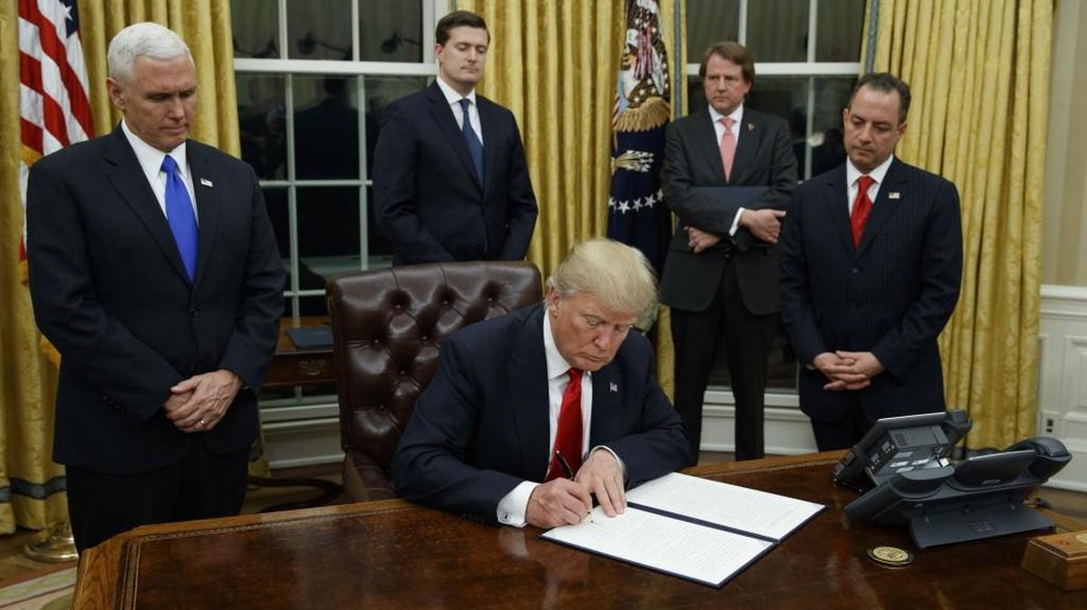 President Donald Trump, flanked by Vice President Mike Pence and Chief of Staff Reince Priebus, signs his first executive order on health care in January.