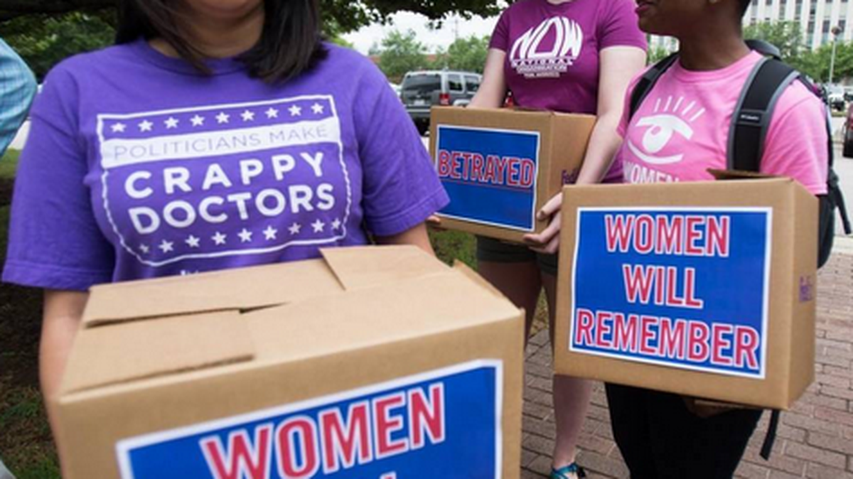 From left, Chavi Koneru, a policy director for NARAL Pro-Choice North Carolina, Maddie Majerus, a volunteer with NARAL Pro-Choice, and Emma Akpan, a field organizer with Planned Parenthood South Atlantic, rally with boxes of signed petition for Gov. Pat McCrory.
