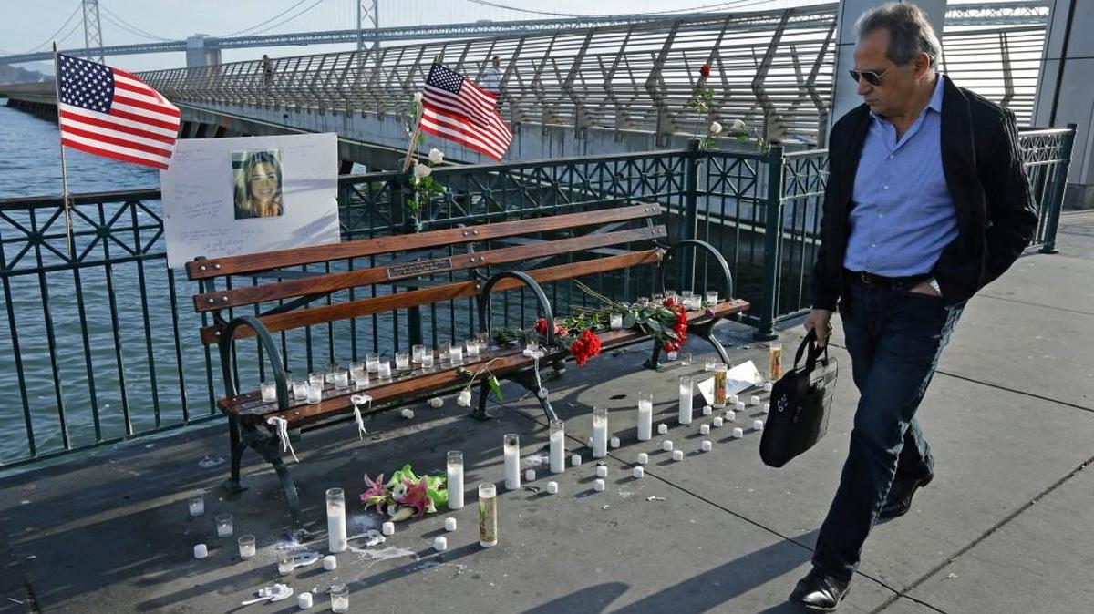A man walks past candles, flowers, and a photo of Kate Steinle at a memorial site on Pier 14 Friday, Dec. 1, 2017, in San Francisco. In this fiercely liberal city, city leaders remained attached to San Francisco's sanctuary city status despite a not guilty verdict in a killing that sparked feverish immigration debates because the man who fired the gun was in the country illegally after being deported five times.