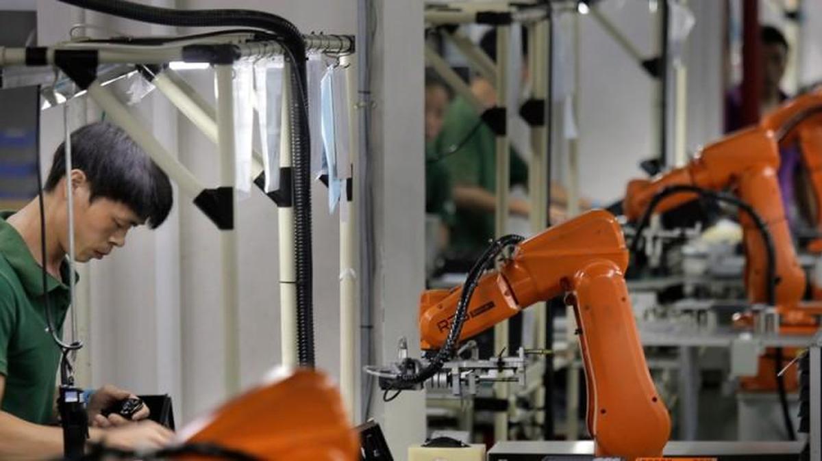 In this Aug. 21, 2015 photo, a Chinese man works amid orange robot arms at Rapoo Technology factory in southern Chinese industrial boomtown of Shenzhen. Factories in China are rapidly replacing those workers with automation, a pivot that’s encouraged by rising wages and new official directives aimed at helping the country move away from low-cost manufacturing as the supply of young, pliant workers shrinks.