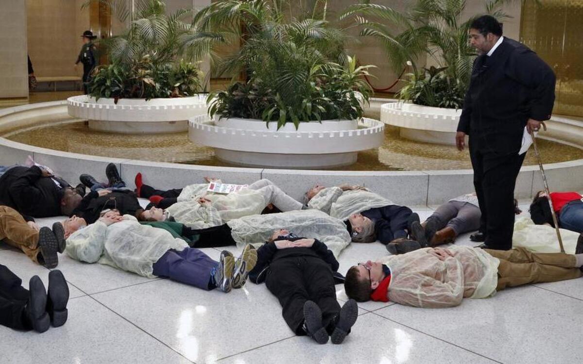 Rev. William Barber, head of the NC NAACP, standing, prays over 13 protesters who participated in a die-in at under the rotunda of the NC Legislature Thursday afternoon, Feb. 12, 2015. The protestors were rallying to protest the state's continued denial of Medicaid expansion for hundreds of thousands of North Carolinians. The protesters were from the NC NAACP and the Forward Together Moral Movement.