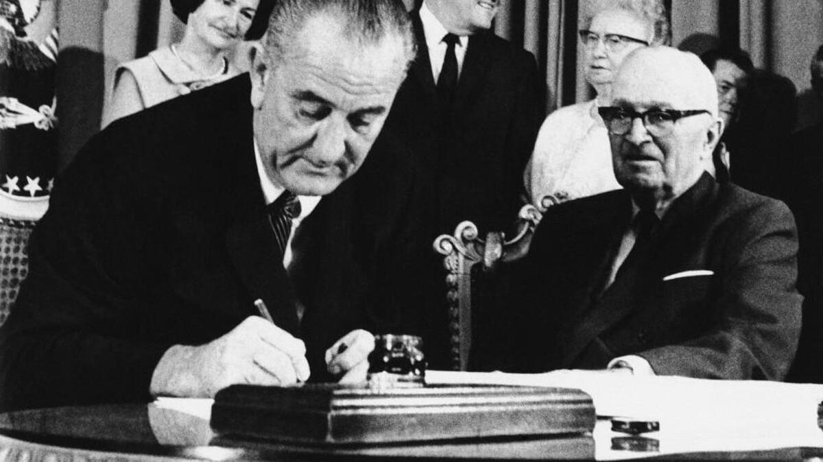 President Lyndon B. Johnson signs Medicare into law on July 30, 1965. At his left is former President Harry S. Truman, the first president to propose national health insurance and the first person to be enrolled in Medicare.