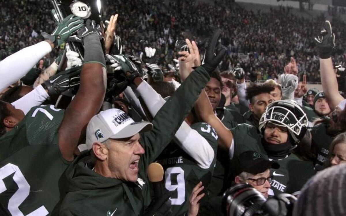 Michigan State coach Mark Dantonio, bottom, and players celebrate with their Big Ten East Division Championship trophy after beating Penn State 55-16 in East Lansing, Mich.