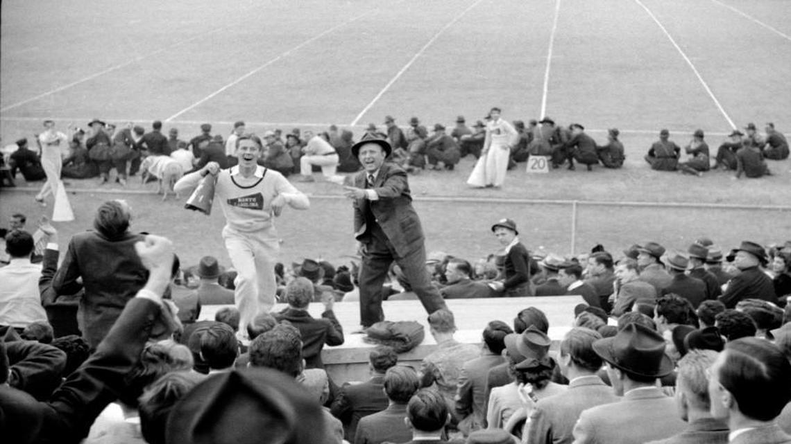 Fans ringed the sidelines and famous bandleader Kay Kyser (right) and a UNC cheerleader lead the crowd in cheers at the 1939 Duke-Carolina game played in Durham. UNC's mascot, Rameses, can be seen just behind the cheerleader.