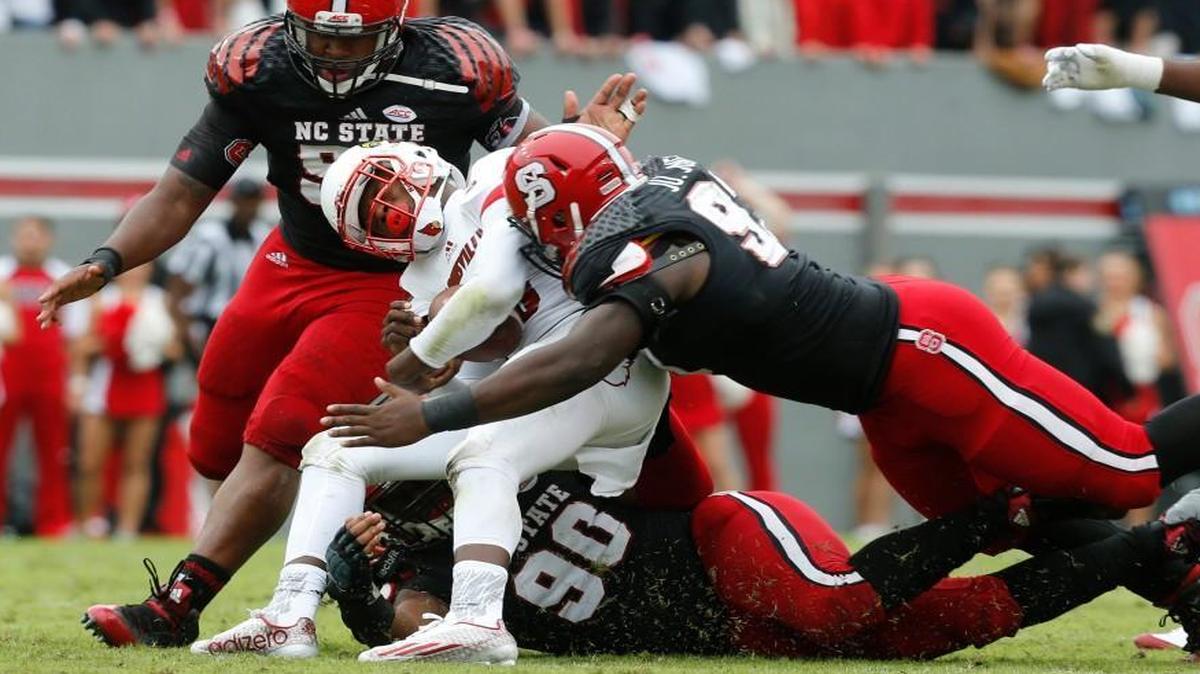 N.C. State's Mike Rose (90), bottom, Justin Jones (93) and B.J. Hill (98) tackle Louisville quarterback Lamar Jackson (8) during the first half of the Wolfpack's game against Louisville at Carter-Finley Stadium in Raleigh, N.C., Saturday, Oct. 3, 2015.