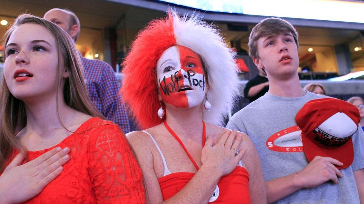 Natalie Miller of Cary, center, along with with niece and nephew Lilly, left, and Avery Underwood, of Newton, N.C., listen as the national anthem is played before N.C. State’s game against Wake Forest in the first round of the ACC Tournament on Tuesday. This is the 22nd ACC Tournament Miller has attended.