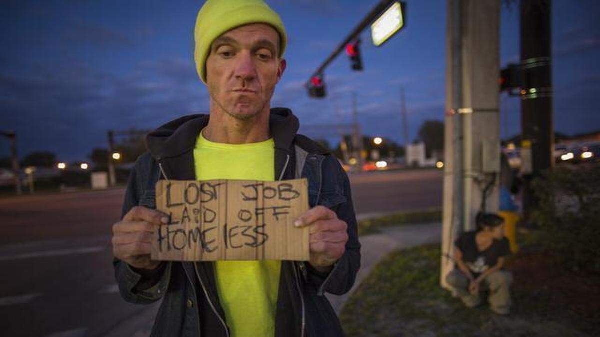 
Ryan Hoffman with a panhandling sign and his girlfriend Michelle Pettigrew, in background, at a busy intersection in Lakeland, Fla., Jan. 7, 2015. Hoffman, once a 287-pound starting left tackle for a top-ten ranked University of North Carolina football team, renowned for his toughness and durability, is now plagued with short-term memory problems and lives on the street, sometimes begging money from passing cars. 
