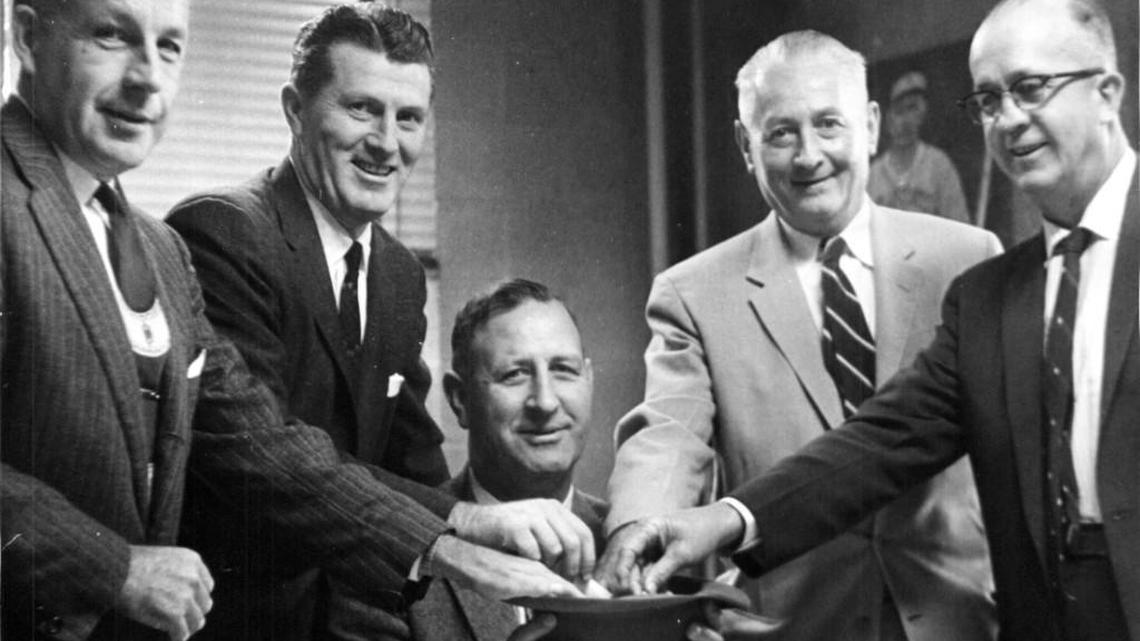 Big Four basketball coaches pull their Dixie Classic opponents from the hat of tournament director Roy Clogston at Reynolds Coliseum in 1957. From left, Harold Bradley, Duke; Frank McGuire, North Carolina; Roy Clogston; Everette Case, NC State; and Murray Greason, Wake Forest assistant athletic director.