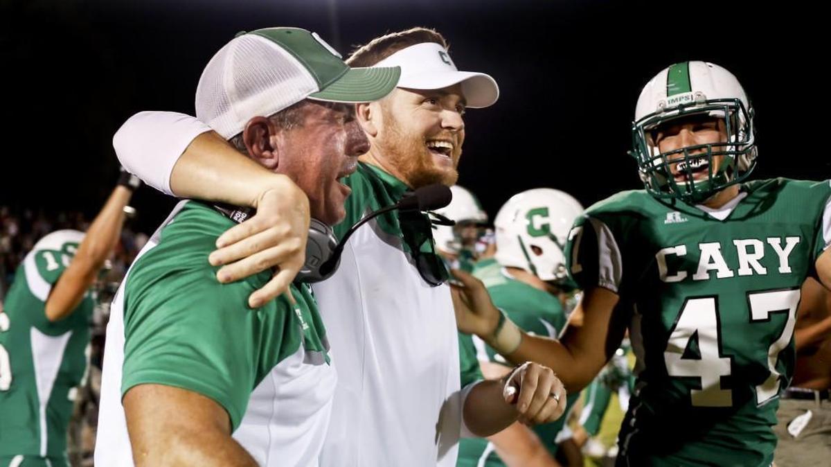 Cary head coach Mike Kirst, center, celebrates with his coaches and players following Broughton's football game at Cary on Friday, August 28, 2015. Cary won the game 10-7.