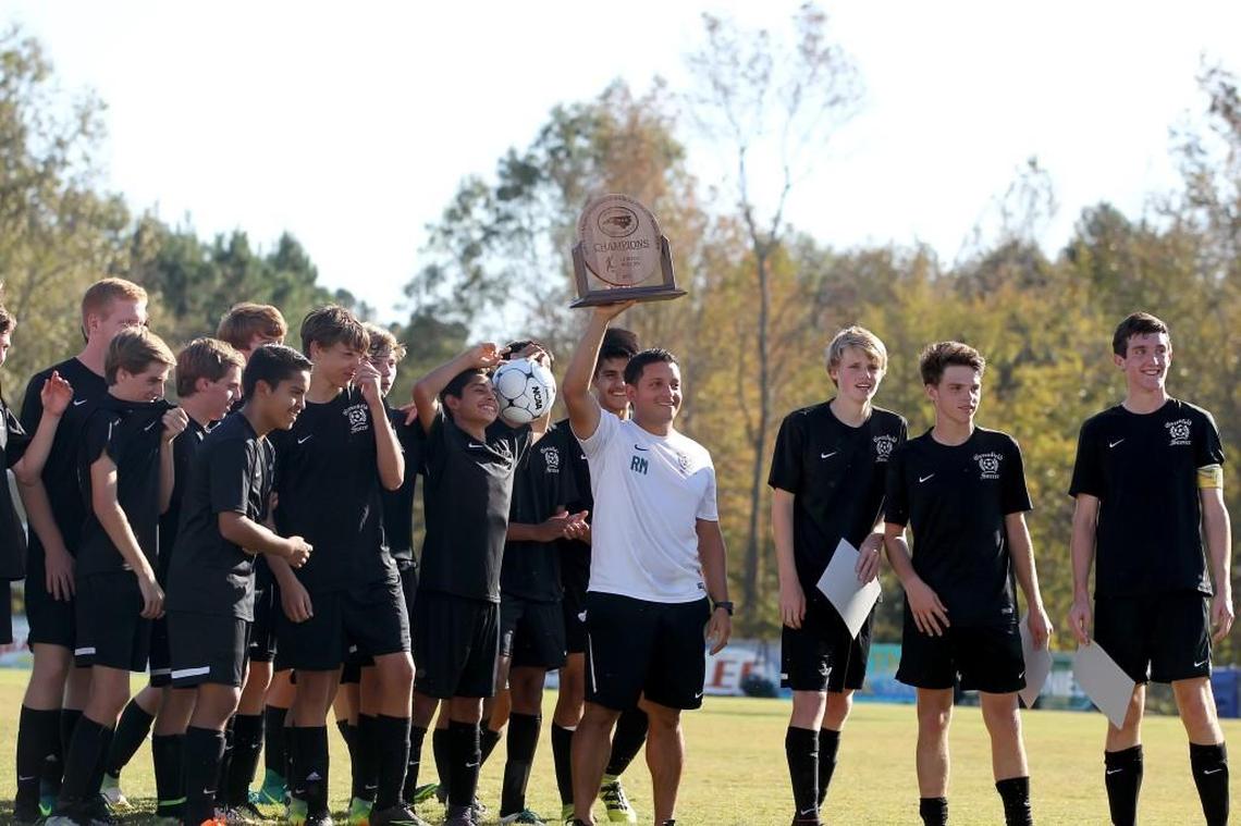 Greenfield coach Randol Mendoza holds the championship trophy high along with members of the Greenfield Knights in the North Carolina Independent Schools Athletic Association 1A Finals. Greenfield School defeated Wayne Country Day School 3-1 in Wilson, N.C. on Saturday, October 29, 2016.