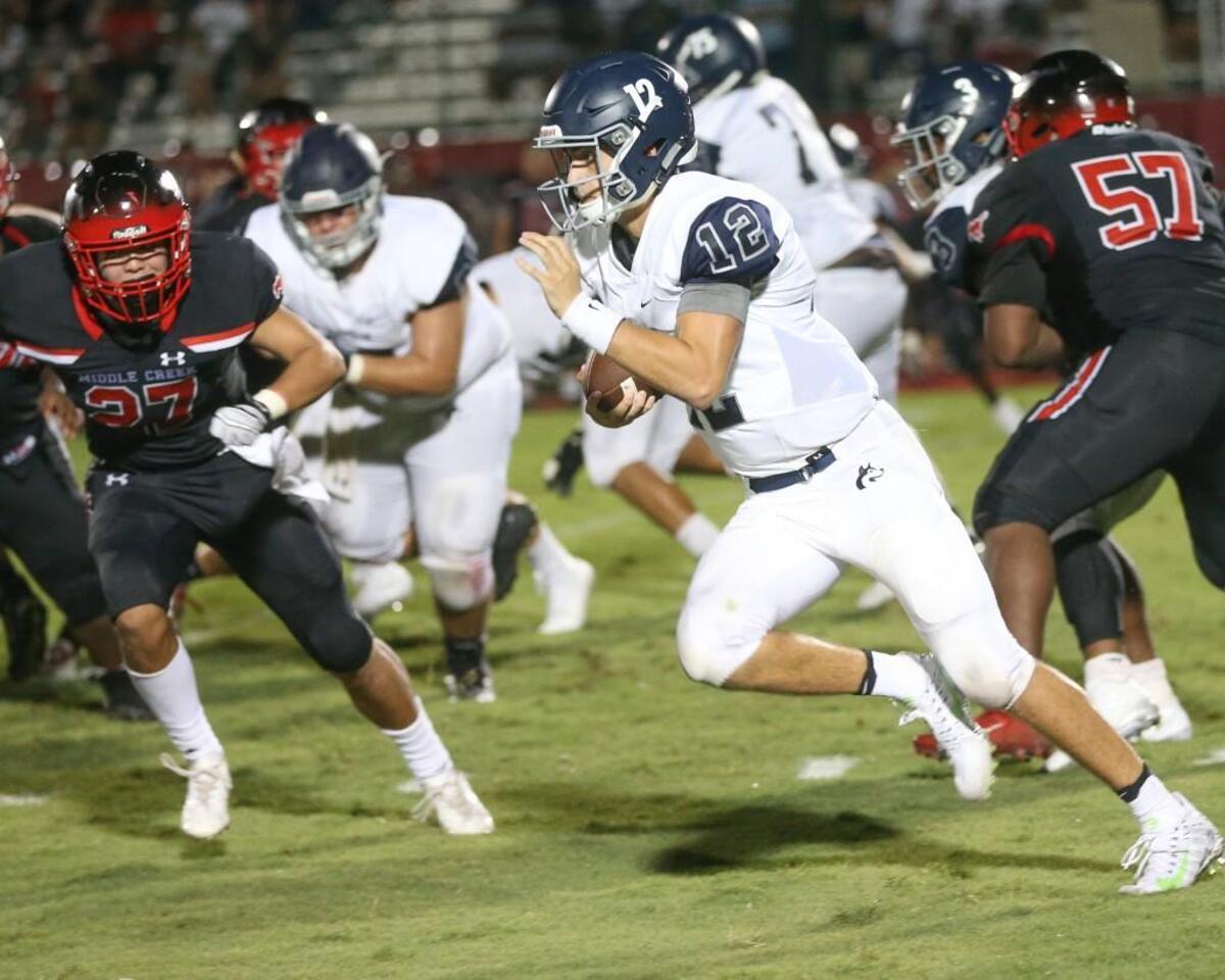 Heritage quarterback Gunnar Holmberg (12) takes the ball around end as Middle Creek's J.J. Tolentino (27) tries to make a stop. Coverage from Heritage Huskies and the Middle Creek Mustangs played in Apex, N.C. on Friday, August 25, 2017. Heritage defeated Middle Creek 47-27.