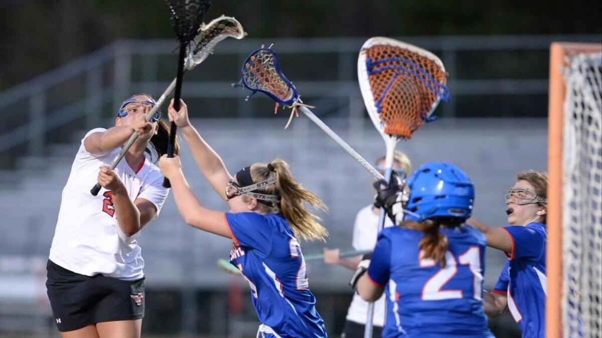 Sam Caputo, left, of Middle Creek scores a goal against Carsin Gronbach, center, and Bridget Nedoma (21) of Athens Drive. The Middle Creek Mustangs played the Athens Drive Jaguars in a girls lacrosse game that took place in Apex, N.C. on Tuesday, March 15, 2016. Middle Creek won 12-7.