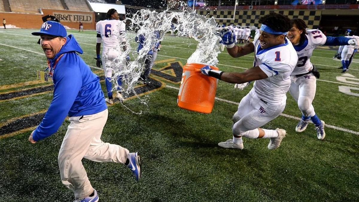 Wake Forest Cougars wide receiver John Jiles, center and wide receiver/tight end Lex Goodwin, right, chase after one of their coaches, left, to douse with water following their victory over the Mallard Creek Mavericks in the 4AA Football State Championship game.