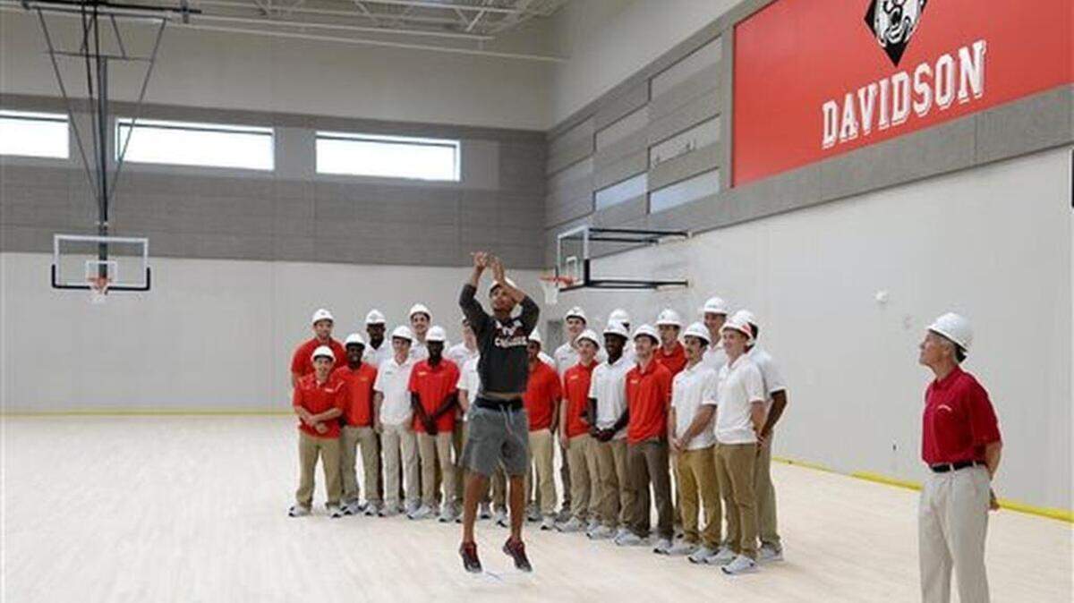 Former Davidson College All-American and NBA All Star Stephen Curry, center, shoots a three-point basket inside Davidson College new basketball practice facility on Thursday, Sept. 17, 2015, as Davidson College men's basketball team and head coach Bob McKillop, right, look on in Davidson, N.C. Curry, of the Golden State Warriors, made a surprise visit to his alma mater, bringing the Larry O'Brien NBA championship trophy along with him to show off. (Jeff Siner/The Charlotte Observer via AP) MAGS OUT; TV OUT; MANDATORY CREDIT