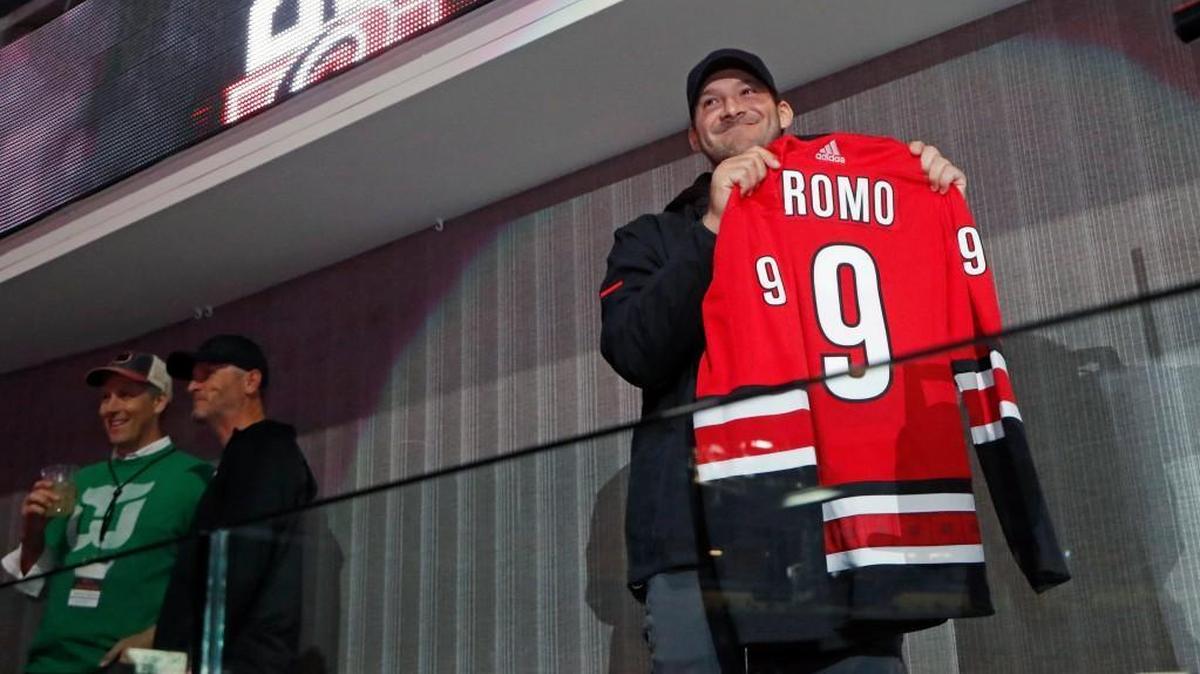 Former Dallas Cowboys quarterback Tony Romo shows his Canes' sweater before he sounds the siren before an NHL game played between the Carolina Hurricanes and the N.J. Devils at PNC Arena in Raleigh, N.C. on March 2, 2018. He is friends with Canes owner Tom Dundon, center.