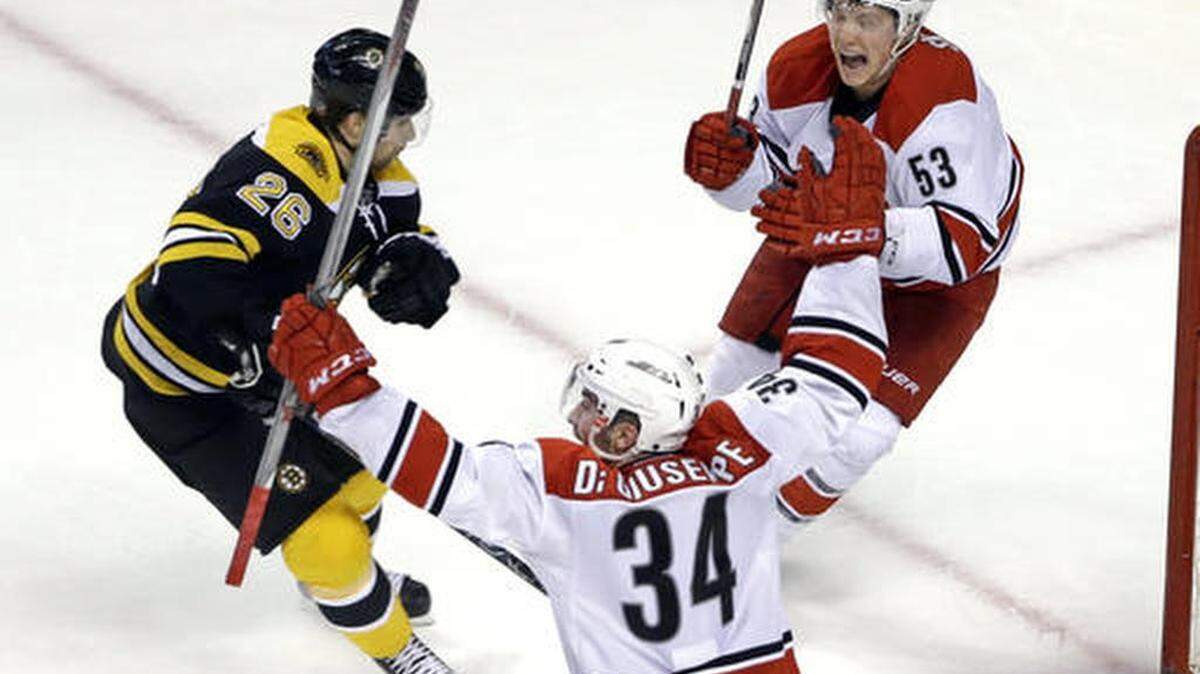 Carolina Hurricanes left wing Phil Di Giuseppe (34) celebrates his winning goal with teammate left wing Jeff Skinner (53) as Boston Bruins defenseman John-Michael Liles (26) watches in the overtime period of an NHL hockey game, Thursday, March 10, 2016, in Boston. The Hurricanes won 3-2.