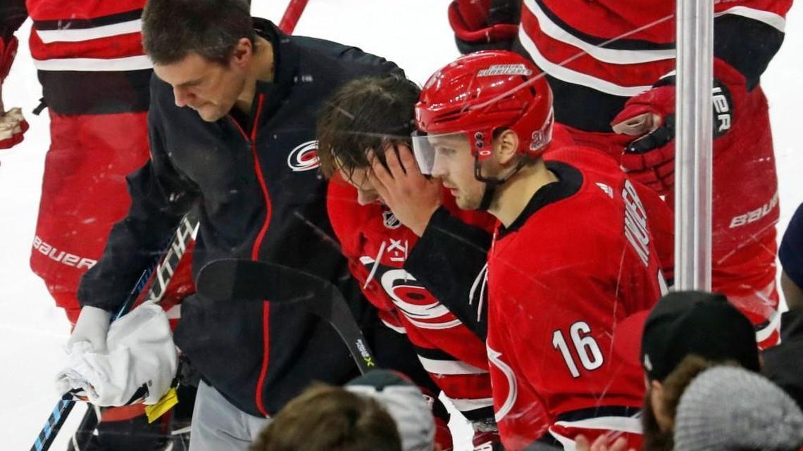 Sebastian Aho, middle, is helped off the ice by trainer Doug Bennett and Marcus Kruger, right, after getting hit by the Flames Mark Giordano on Sunday.