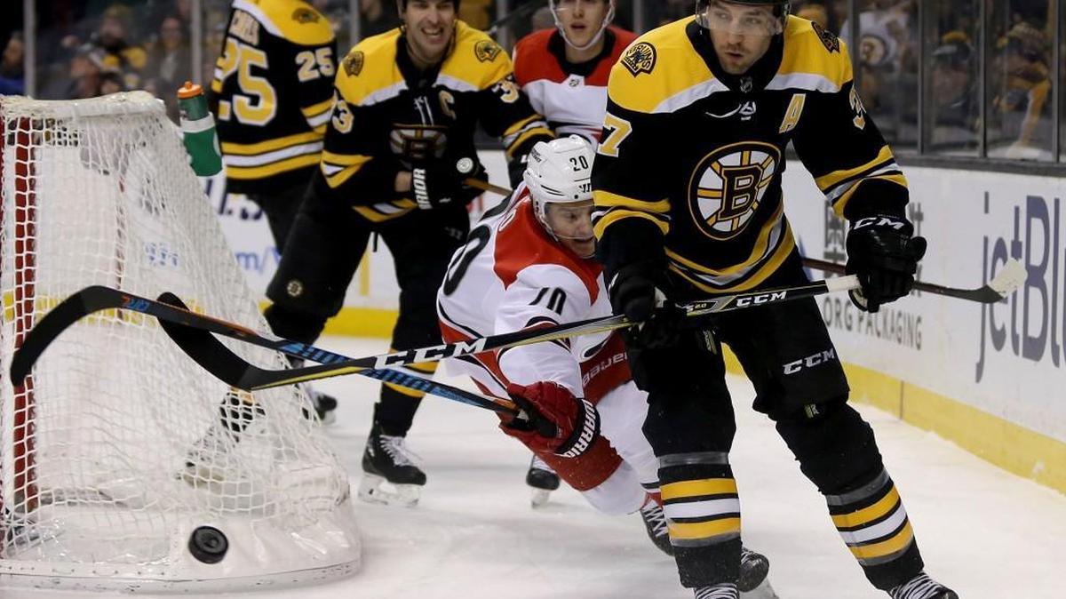 Boston Bruins center Patrice Bergeron (37) looks to clear the puck from behind the net as Carolina Hurricanes right wing Sebastian Aho (20) lunges to deflect it during the first period of an NHL hockey game Saturday, Jan. 6, 2018, in Boston. Aho later left the game with a lower-body injury; Sunday the Hurricanes said his status was "day to day."