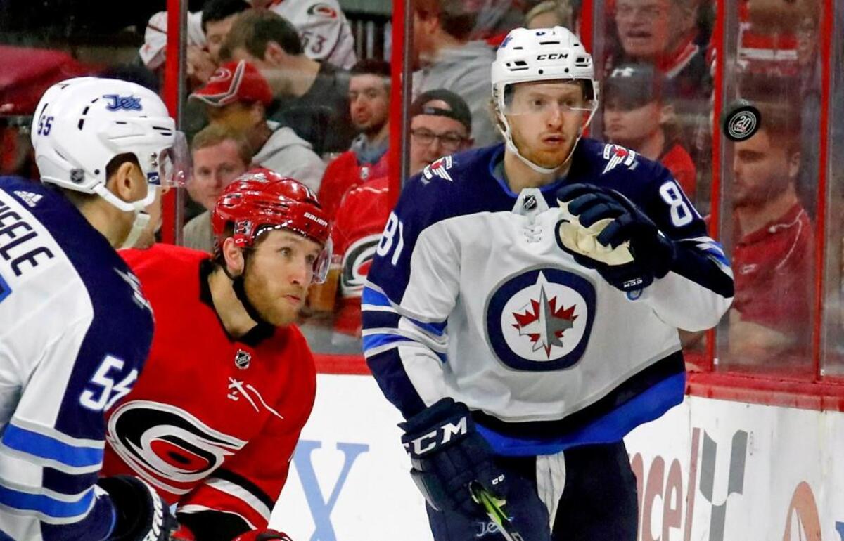 The Jets' Mark Scheifele (55) and Kyle Connor (81) and the Canes' Jaccob Slavin (74) keep their eyes on a flying puck during the second period.