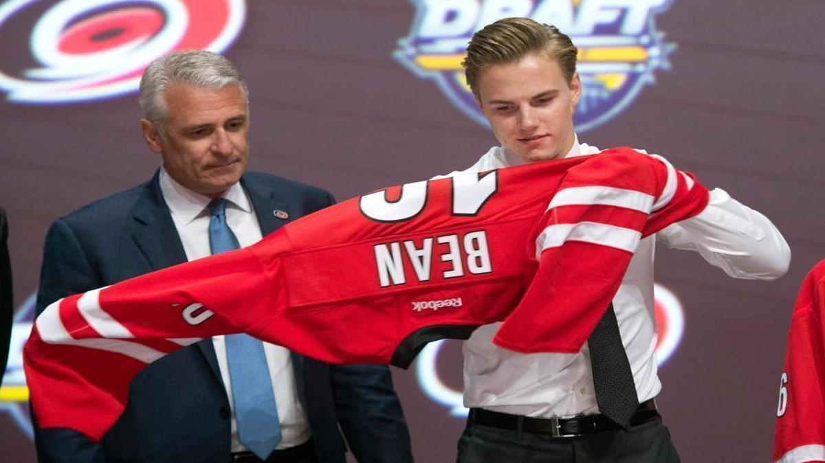 Jake Bean, right, puts on a Carolina Hurricanes sweater as Canes general manager Ron Francis looks on at the NHL hockey draft in Buffalo, N.Y. He was taken as the 13th player in the first round of the draft.
