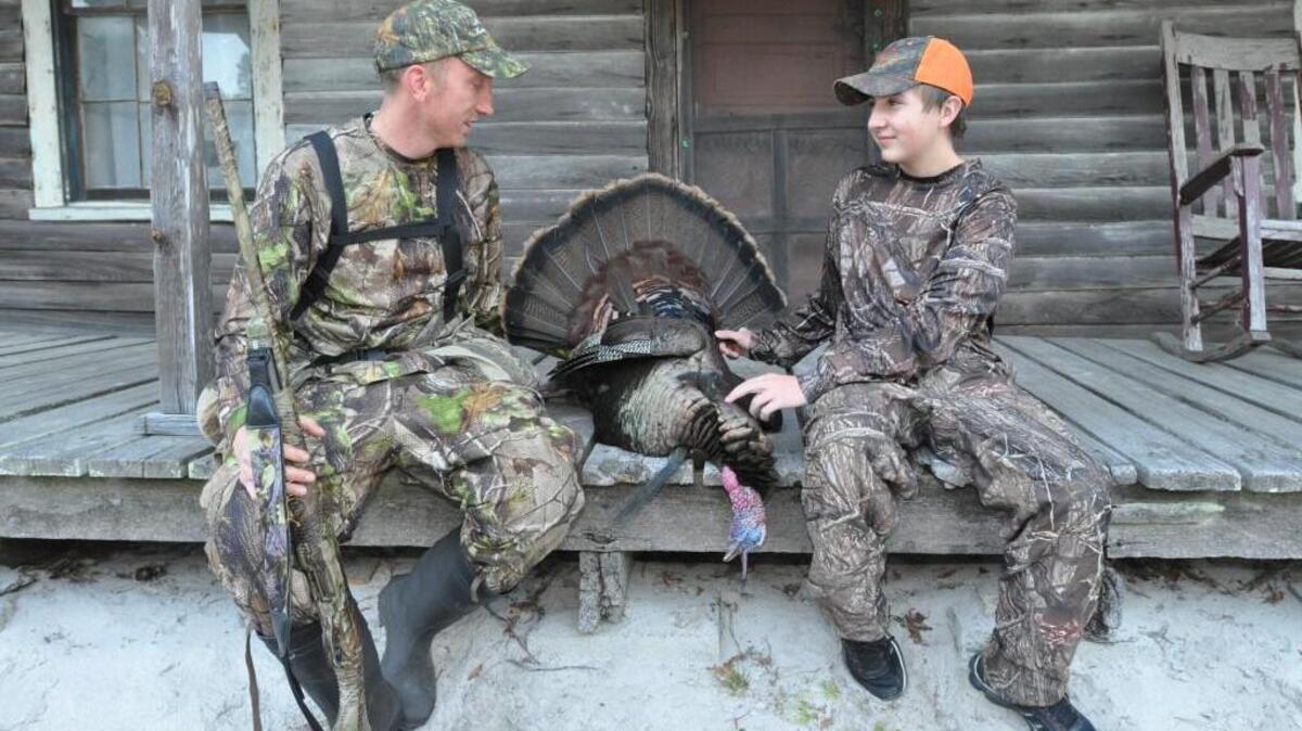 Mike Wiston (left) tells Hunter Martin about his successful turkey hunt on the porch of a hunting cabin in Pender County.